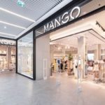 Witryna sklepowa sieci Mango. Wejście do salonu w centrum handlowym. Nad przejściem znajduje się duży logotyp marki.