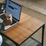 Mężczyzna siedzący przed laptopem robiący zakupy online e-commerce z kartą kredytową w dłoni