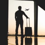 Mężczyzna na lotnisku z walizką, odlatujący samolot w tle, bagaż podręczny