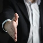 Mężczyzna w białej koszuli i czarnej marynarce wyciąga dłoń