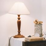 Lampa stołowa z abażurem na stoliku nocnym z dekoracyjnymi rzeźbami i książką