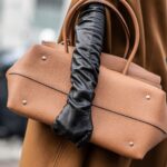 Kobieta w brązowym płaszczu, czarnych rękawiczkach i z brązową torebką-shopperką