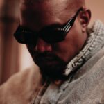 Adidas i Kanye West. Krótko ostrzyżony, czarnoskóry mężczyzna w czarnych okularach. Ma on na sobie niebieską, jeansową kurtkę.