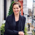 Anne Applebaum, żona Radosława Sikorskiego, ubrana w granatowy kardigan spod którego wystaje czarny top. Uśmiechnięta kobieta, krótko przystrzyżona o ciemnobrązowych włosach.