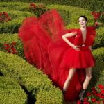 Kolekcja H&M z Giambattista Vallim. Kobieta w czerwonej sukience w ogrodzie z labiryntem.