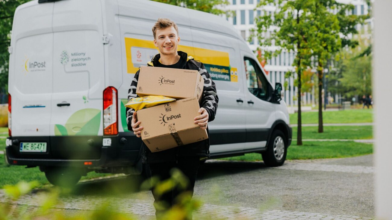 Kurier InPost niosący przesyłki do urządzenia Paczkomat®. Za nim stoi samochód kurierski.