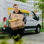Kurier InPost niosący przesyłki do urządzenia Paczkomat®. Za nim stoi samochód kurierski.