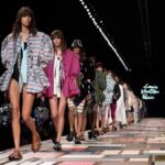 Pokaz Louis Vuitton, domu mody będącego przedstawicielem malejącego rynku dób luksusowych. Na zdjęciu widzimy catwalk, po których przechodzą modelki. Większość z nich ubrana jest w krótkie szorty oraz kolorowe koszulce i oversizowe marynarki.
