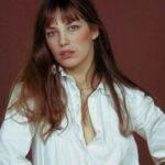 Jane Birkin w białej koszuli na białym tle. Ma rozpuszczone włosy.