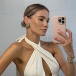 Maja Bohosiewicz PLNY Lala - influencerka miała zostać oszukana na 1,5 miliona złotych. Na zdjęciu Maja Bohosiewicz ubrana w białą sukienkę, robi sobie zdjęcie telefonem w lustrze. Ma spięte blond włosy i duże kolczyki.
