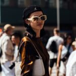 Vinted pesel. Na zdjęciu modelka w ciemnych okularach z białym oprawkami oraz w czarnym kaszkiecie Kangol.