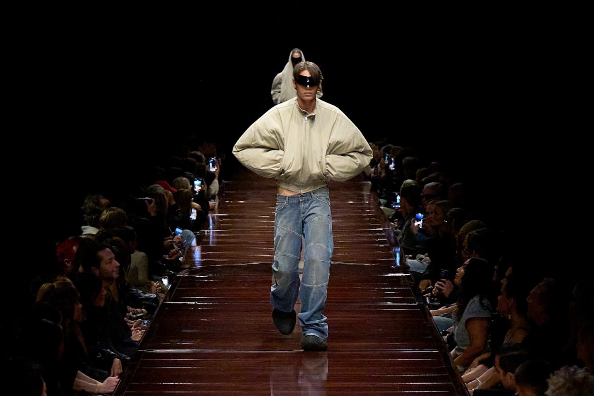 Kadr z pokazu mody marki Balenciaga. Mężczyzna kroczy przez catwalk w oversize'owych jeansach oraz białej kurtce. Czy z tego obrazu można wyciągnąć wskazówki dla polskich marek na 2025 rok?