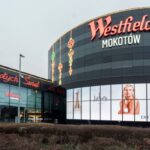 Zdjęcie przedstawia fasadę centrum handlowego Westfield Mokotów w Warszawie, ozdobioną świątecznym napisem „Wesołych Świąt” oraz reklamą perfum Dior. W tle pojawia się slogan „napad w galerii mokotów”, który przykuwa uwagę i stanowi nawiązanie do potencjalnego zdarzenia w tej lokalizacji.