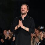 Matthieu Blazy nowy dyrektor kreatywny Chanel. Na zdjęciu uśmiechnięty projektant po pokazie SS2023, składający dłonie w dziękczynnym geście, ubrany w czarną koszulę.