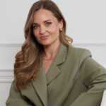 Właścicielka Luare. Długowłosa Monika Frydrych znajduje się na tle białej ściany Ubrana jest w zieloną, oversize'ową marynarkę. Kobieta ma ciemną karnację. Jej stylizację podkreśla biżuteria.