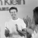 Calvin Klein podczas jednego ze swoich pokazów, oklaskiwany przez publiczność. Ubrany jest w biały T-shirt.