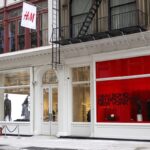 H&M płatne zwroty online - cennik. Na zdjęciu fasada sklepu H&M w Nowym Jorku. Na górze wiszą flagi z logo H&M. Elegancki sklep posiada charakterystyczną czerwoną szybę na jednej z witryn.