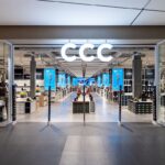 CCC przejmuje udziały w Szopex. Wejście do nowoczesnego sklepu CCC, z dużym, podświetlanym logo nad drzwiami, ukazujące przestronne wnętrze z regałami pełnymi obuwia i akcesoriów.