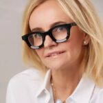 Joanna Czech, kosmetyczka gwiazd. Zbliżenie na kobietę w blond włosach, w białej koszuli i charakterystycznych okularach korekcyjnych w mocnych czarnych oprawkach.