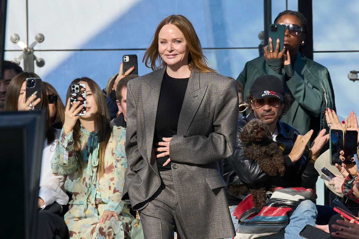 Stella McCartney wykupuje udziały od LVMH i odzyskuje kontrolę nad firmą. Projektantka w eleganckim oversize'owym garniturze na pokazie mody, otoczona publicznością, z której wiele osób robi zdjęcia telefonami.