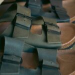 Czy tańsze zamienniki Birkenstock mogą być legalnie sprzedawane? Zbliżenie na klapki Birkenstock, wykonane z ciemnozielonej skóry z czarnymi klamrami i korkową podeszwą. Klapki ułożone są na półce, ukazując detale materiału i strukturę pasków.