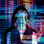 Agenci AI i agentic AI - czy zrewolucjonizują modę? Kobieta stoi w ciemnym otoczeniu, na jej twarz i ciało rzutowane są cyfrowe obrazy przedstawiające kod komputerowy, liczby binarne i kolorowe linie symbolizujące dane. Obraz tworzy futurystyczny i technologiczny klimat, sugerując tematykę sztucznej inteligencji, cyberbezpieczeństwa lub przetwarzania danych.