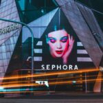 Sephora Kids. Zdjęcie przedstawia budynek sklepu Sephora nocą. Oprócz szyldu marki widać reklamę z kobietą z kolorowym makijażem oczu.