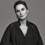 Francesca Amfitheatrof. Czarno-białe zdjęcie projektantki, związanej do niedawna z Louis Vuitton. Kobieta pozuje w luźnej ciemnej koszuli i spiętych włosach.
