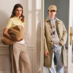 Modivo odpowiada na trendy wiosna lato 2025. Młoda kobieta i mężczyzna w eleganckim, casualowym stylu pozujący w jasnym, klasycznie urządzonym wnętrzu. Kobieta nosi żółtą koszulkę polo, wzorzyste spodnie i trzyma beżową kurtkę. Mężczyzna ubrany jest w beżowy płaszcz, szarą bluzę z grafiką misia, jasne jeansy i czapkę z daszkiem. Oboje mają spokojne, poważne wyrazy twarzy.