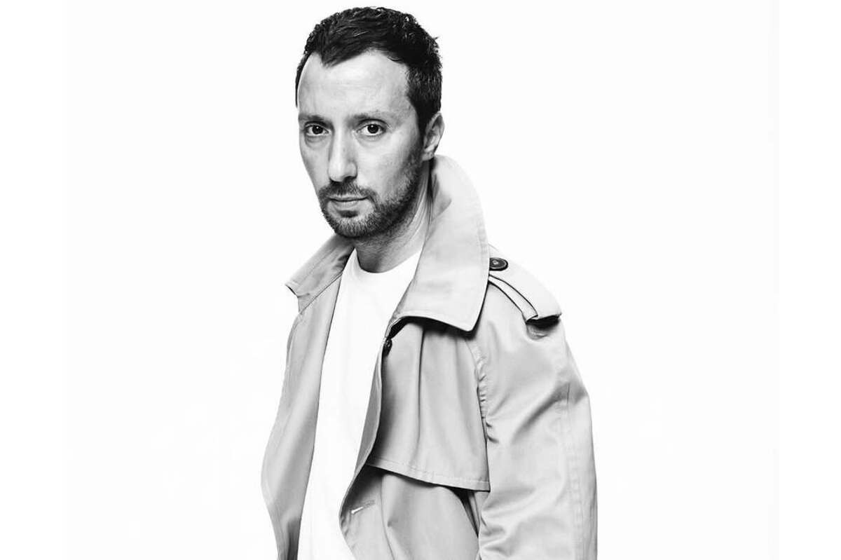 Anthony Vaccarello – czarno-białe zdjęcie dyrektora kreatywnego YSL. Mężczyzna ma ciemne włosy, nosi białą koszulkę i trencz.