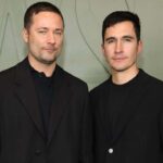 Jack McCollough i Lazaro Hernandez z Proenza Shouler – kariera, życiorys, współprace. Zdjęcie przedstawia portret dwóch mężczyzn: projektantów Jacka McCollougha i Lazaro Hernandeza. Mężczyźni pozują na tle zielonej ściany, są ubrani w czarne koszulki i marynarki w tym samym kolorze.