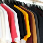 Monnari przejmuje 5.10.15. Na zdjęciu rząd kolorowych koszulek na wieszakach, odcienie od bieli, czerwieni i czerni po żółcie, brązy i granaty, uporządkowane w szafie lub sklepie odzieżowym.