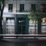 Zdjęcie sklepu Nike nocą, zrobione z długą ekspozycją. Widać na nim wejście do sklepu z logo marki i stojącego przed nim mężczyznę.