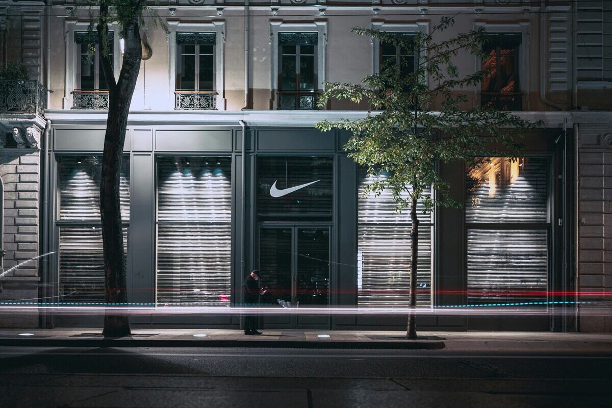 Zdjęcie sklepu Nike nocą, zrobione z długą ekspozycją. Widać na nim wejście do sklepu z logo marki i stojącego przed nim mężczyznę.