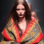 Pola Dzik - młoda polska modelka, która otworzyła pokaz Versace. Na zdjęciu modelka na wybiegu ubrana w puchowy płaszcz we wzory Versace.