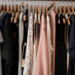 Gerry Weber upada po raz kolejny. Wnętrze sklepu odzieżowego z eleganckimi ubraniami na drewnianych wieszakach – delikatne tkaniny w pastelowych i ciemnych barwach. Zdjęcie ilustruje kryzys niemieckiej marki modowej znanej z klasycznego stylu.