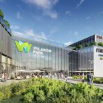 Wizualizacja nowego centrum handlowego Wilanów Park w Warszawie. Nowoczesny budynek z przeszkloną fasadą i zielonymi tarasami. Na elewacji widoczne logo „Wilanów Park” oraz nazwy sklepów. Przed wejściem przestrzeń z roślinnością, kawiarniami i spacerującymi ludźmi.