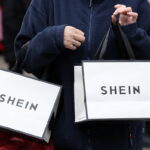 Shein i Temu – podwyżki cen. Zdjęcie przedstawia klientkę niosącą torby z gadżetami promocyjnymi Shein. Torebki są białe z czarnymi detalami.