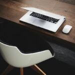Wielki Czwartek 2025 wolne od pracy? Na zdjęciu miejsce pracy - krzesło biurowe z czarną wyściółką oraz laptop i myszka ustawione na drewnianym biurku.