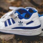 Adidas wyciek danych - kto jest poszkodowany? Na zdjęciu białe sneakersy adidas z niebieskimi paskami, zapinane na rzepy.