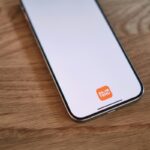 Zdjęcie telefonu leżącego na drewnianym blacie. Ekran jest biały, na dole wyświetla się pomarańczowe logo Temu – chińskiej platformy, której UOKiK postawił zarzuty.