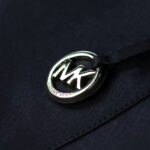 Ceny torebek Michael Kors wzrosną. Na zdjęciu Michael Kors logo srebrne metalowe.