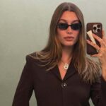Hailey Bieber robi selfie w okularach przeciwsłonecznych i brązowej marynarce. Jej telefon ma etui z balsamem do ust marki Rhode, która trafi do Seephory.