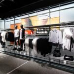 Wnętrze sklepu Nike z widocznymi wieszakami i manekinami z odzieżą, obuwiem i akcesoriami amerykańskiej marki. Całość jest utrzymana w nowoczesnym stylu.