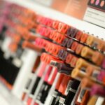 Drogeria Pigment upadłość i śmierć właściciela. Co dalej z kultową drogerią z Krakowa. Na zdjęciu półka w sklepie z kosmetykami, na której znajdują się rzędy kolorowych błyszczyków lub pomadek w tubkach, ustawionych w uporządkowany sposób. Kolory obejmują różne odcienie różu, czerwieni, brązu i pomarańczu.