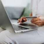 Amazon Haul - nowa platforma zakupowa rusza w Europie. Co zaoferuje? Osoba siedząca na kanapie korzysta z laptopa marki Apple, trzymając w ręce kartę kredytową – ilustracja przedstawiająca zakupy online lub płatność internetową.