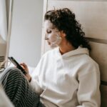 Rossmann wprowadza nowy system promocji. Zegar odmierza czas. Na zdjęciu kobieta w maseczce na twarzy siedzi przeglądając telefon.