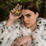 Modelka z perfumami Avon – firmy kosmetycznej, która rozwija model franczyzowy w Polsce. kobieta ma ciemne spięte włosy, nosi białe futro w czarne kropki.