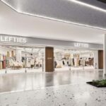 Zdjęcie sklepu Lefties, który należy do holdingu Inditex i jest nazywany "siostrą Zary" lub "tańszą Zarą". Fotografia jest utrzymana w białej kolorystyce, widać na niej świecący się szyld z napisem marki, wejście do sklepu i wieszaki z ubraniami.