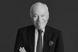 Leonard Lauder. Czarno-biały porter syna założycieli marki Estée Lauder. Mężczyzna uśmiecha się, ma siwe włosy oraz nosi garnitur z białą koszulą i ciemnym krawatem. Z kieszeni marynarki wystaje poszetka.